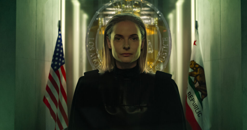 A stern-looking figure dressed in black stands before a backdrop of the American and California flags, with a glowing emblem of justice behind them, creating an atmosphere of authority and intrigue.